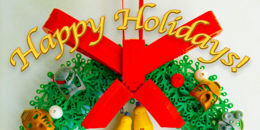 "Happy Holidays!" over a LEGO wreath creation featuring a large red bow, 2 bells, and gold and silver Toa Mata masks.